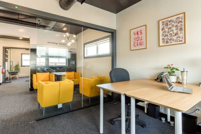 Bureau loft avec table et fauteuils jaunes séparés par une cloison vitrée