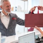 Une entrepreneure remet un sac à un client souriant, dans un local lumineux